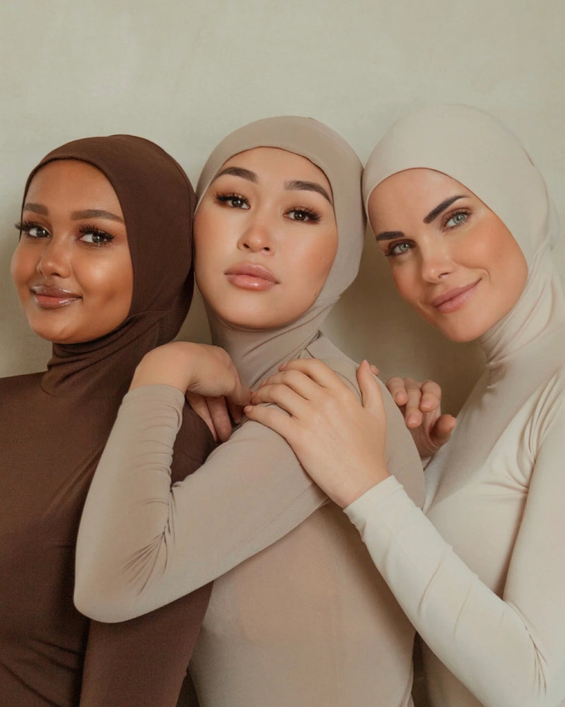 Three women wearing hijab bodysuit of different colors, hugging each other
